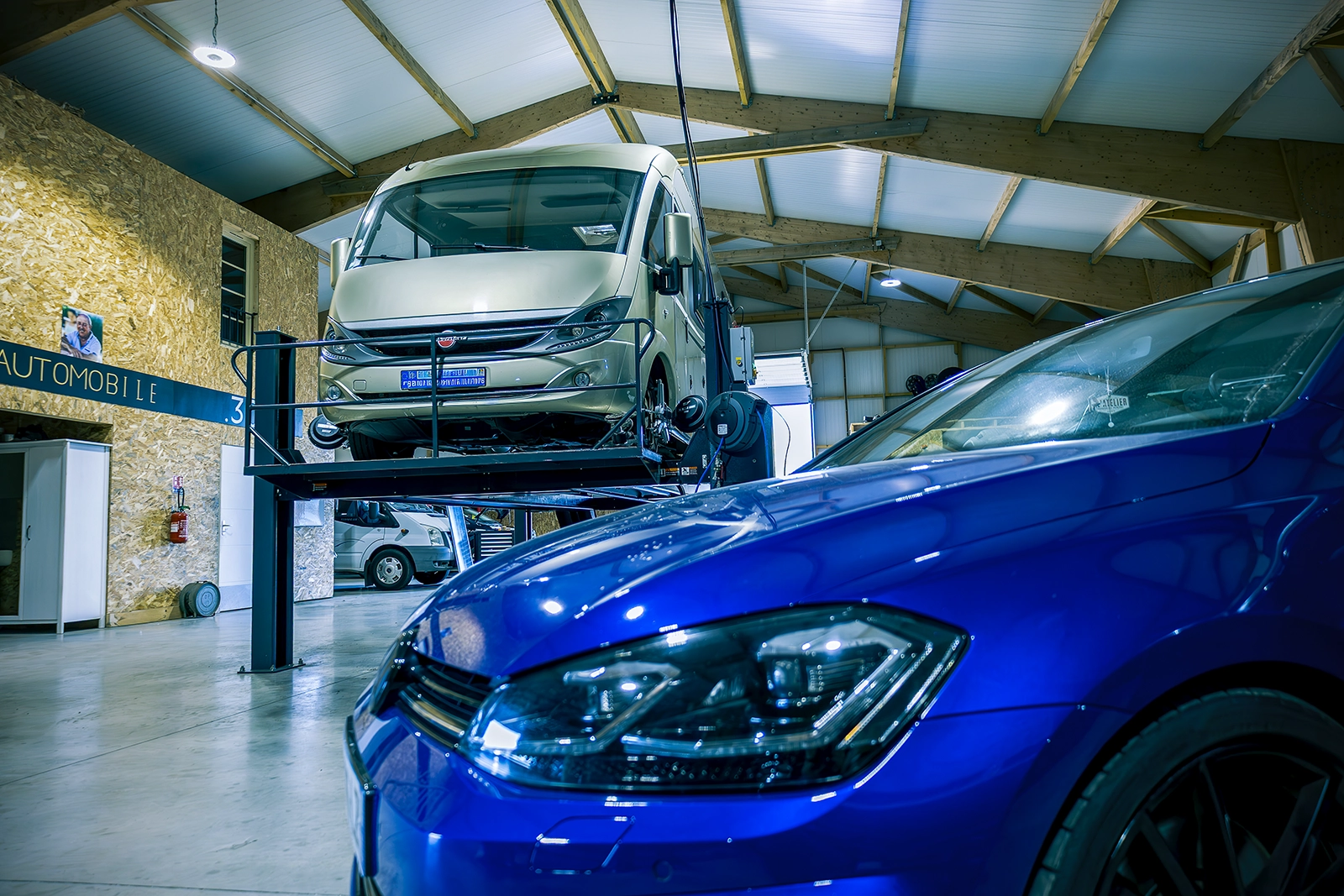 Camping car sur un pont dans un garage avec une voiture en premier plan
